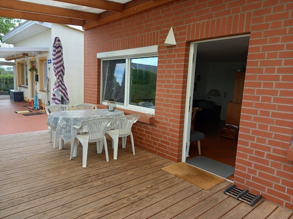 A covered patio with a table and chairs, a brick wall, and a door leading inside.