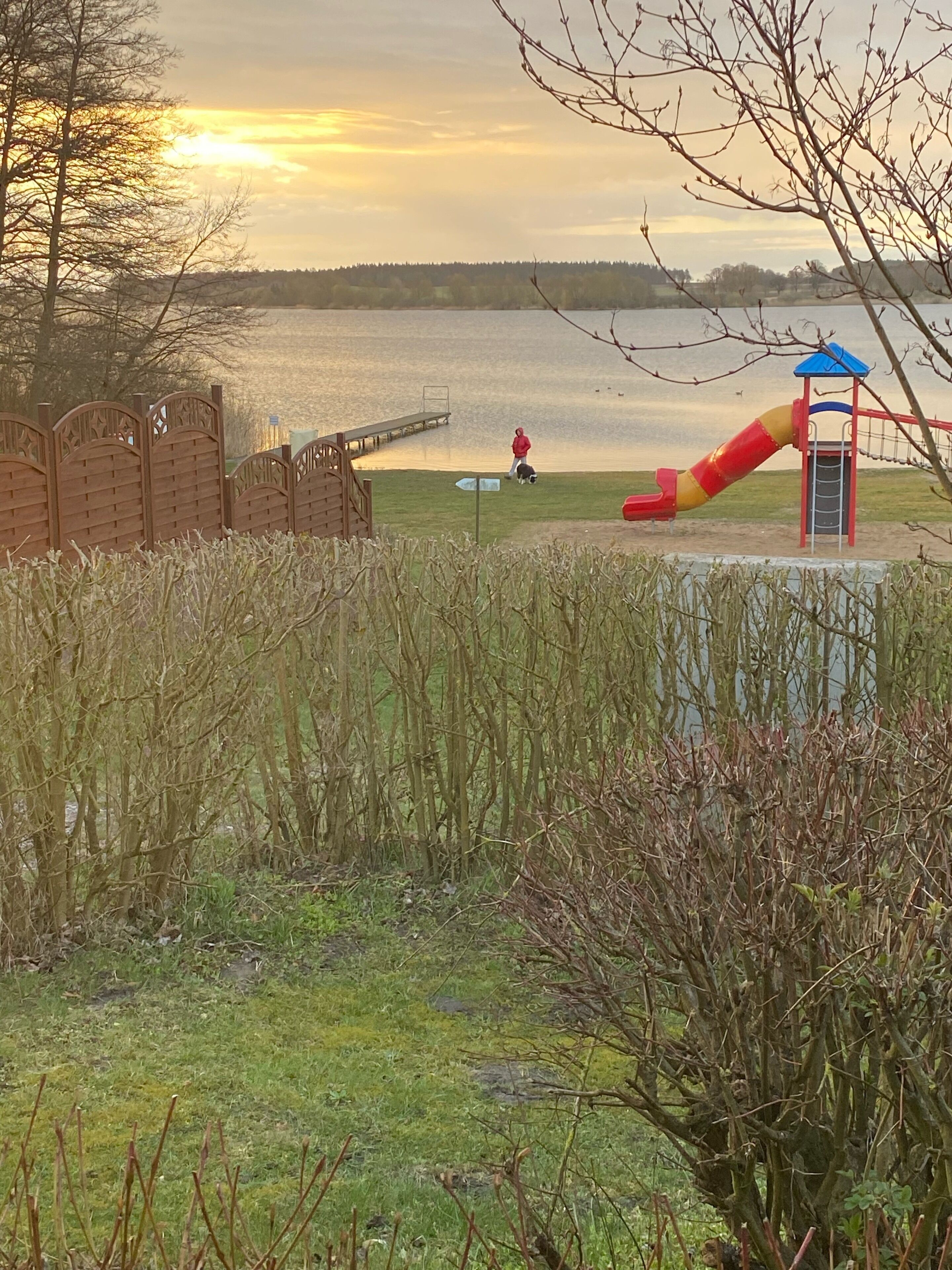 A park with a playground, a wooden fence, and a body of water in the background.