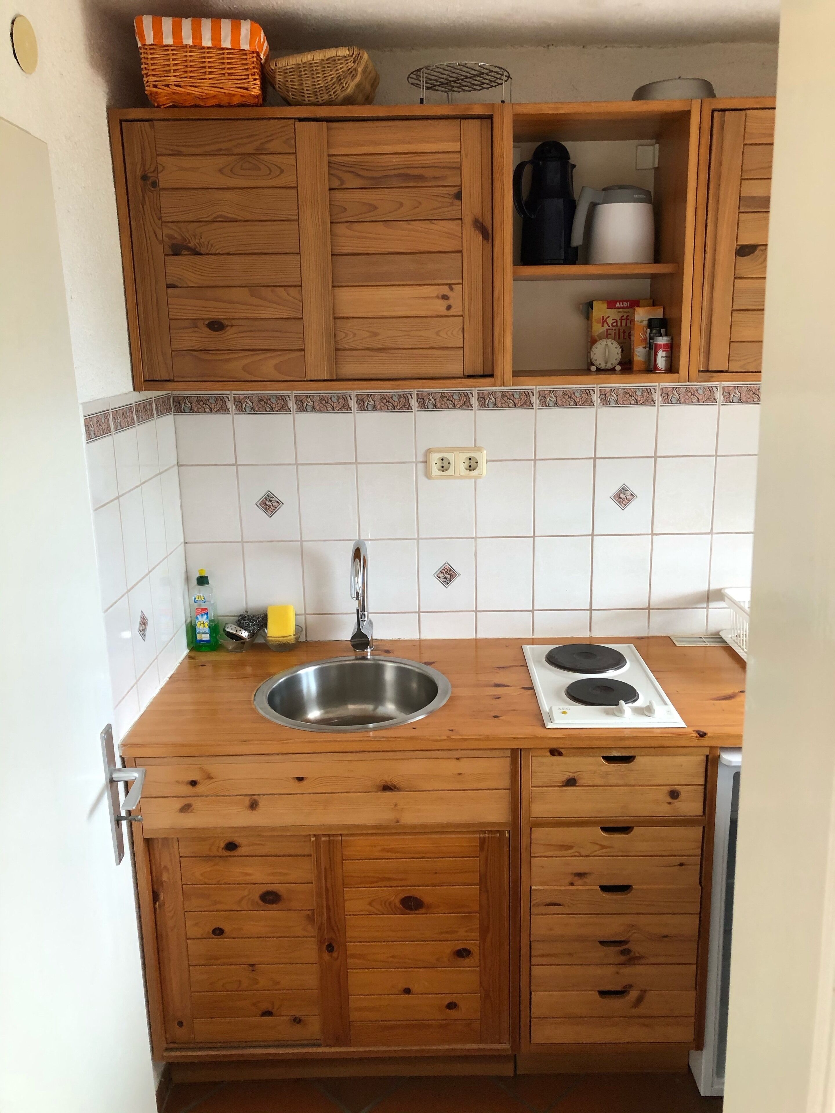 Una cocina con armarios de madera, un lavamanos de acero inoxidable, una estufa y un salpicadero de azulejos.