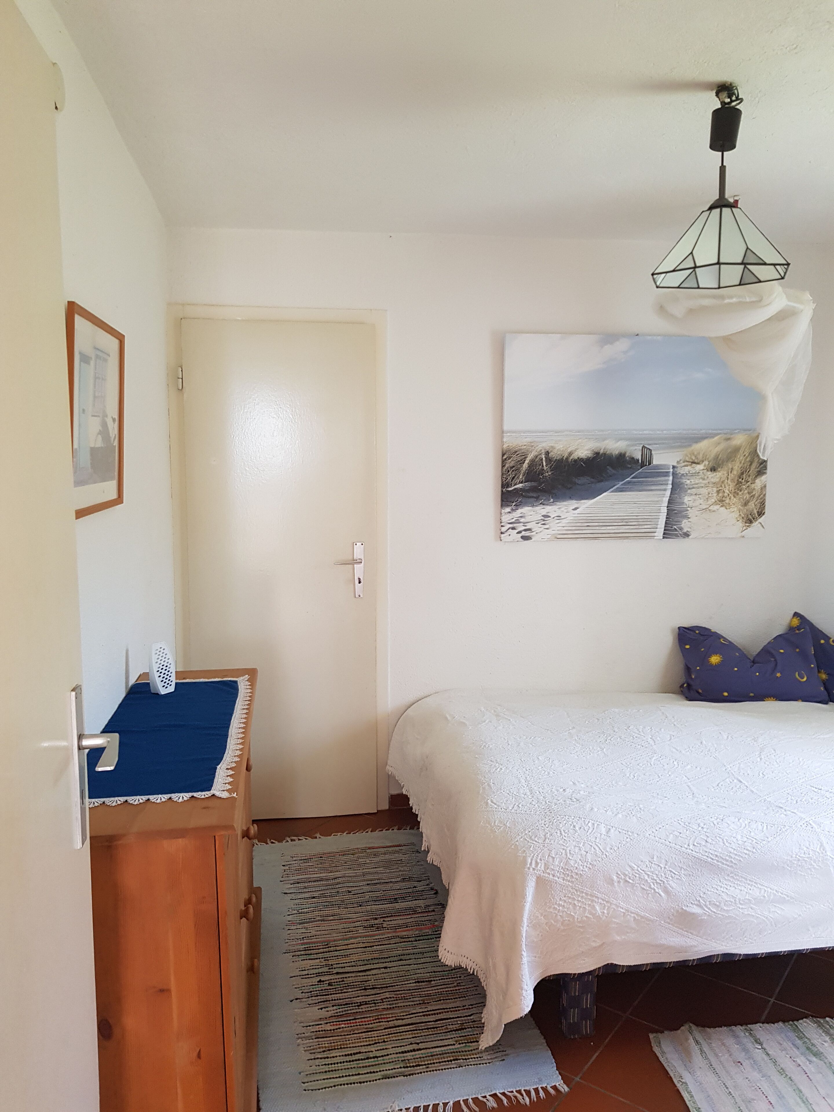 Una camera da letto con un letto, un comò in legno, una porta, un quadro appeso al muro e un lampadario.