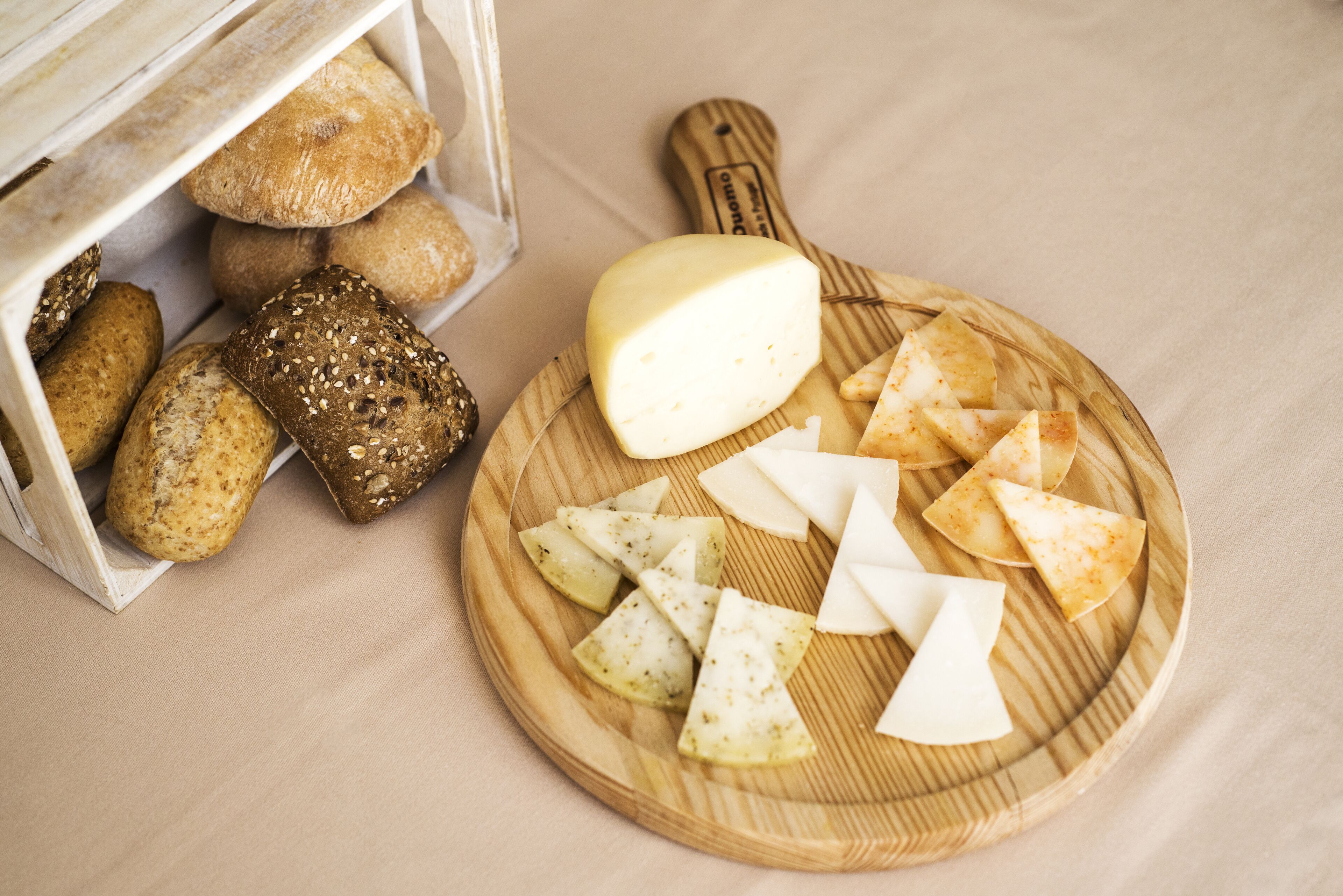 A wooden cutting board with cheese, sliced bread, and crackers on a table.