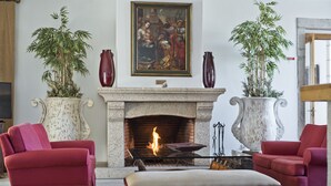 A living room with a fireplace, two red sofas, a white ottoman, and two large potted plants. - Lam Hotel Convento do Desagravo (Oliveira do Hospital)