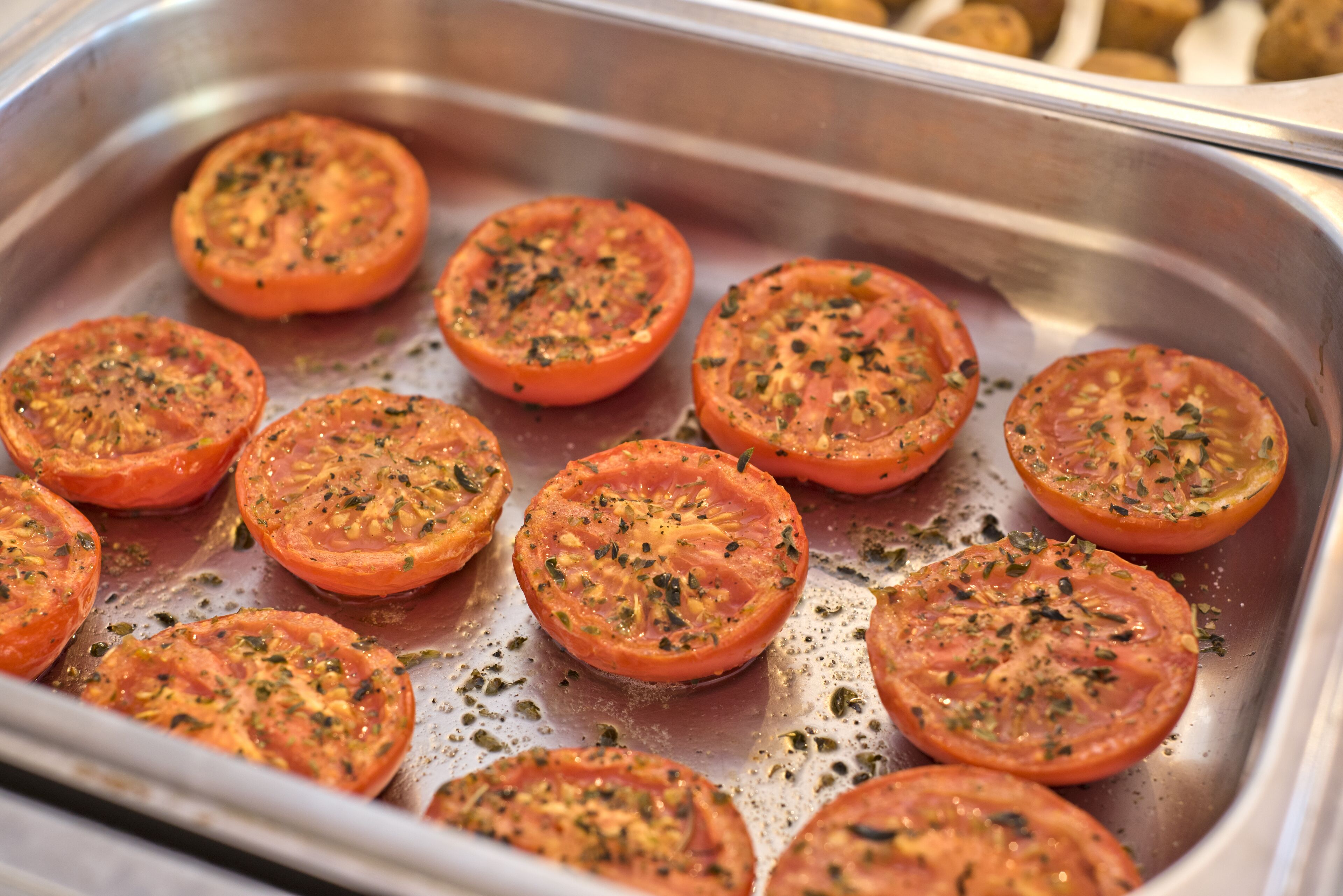 A stainless steel tray with sliced tomatoes seasoned with herbs.