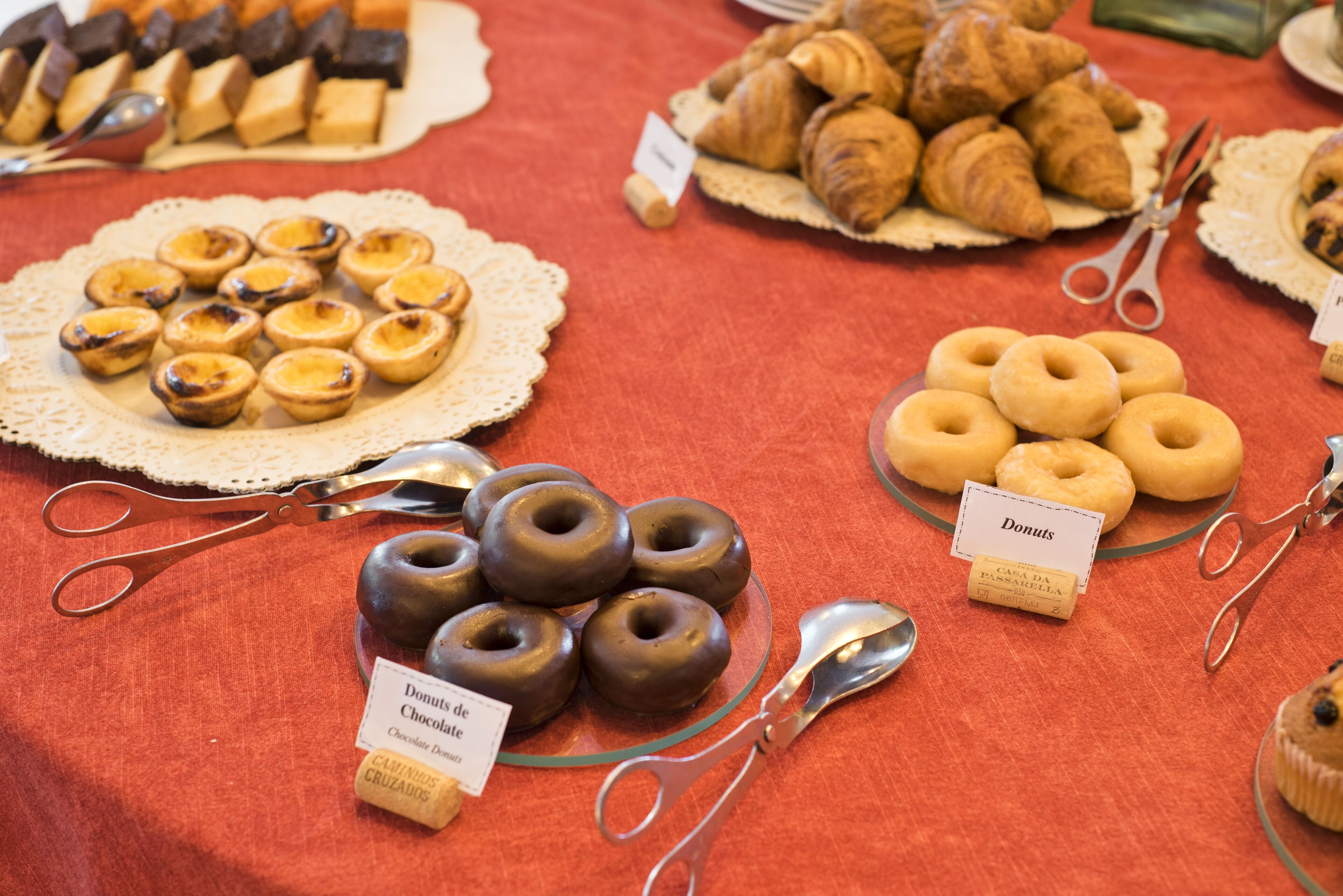 A table with various pastries including chocolate donuts, croissants, and tarts, each labeled with their names.