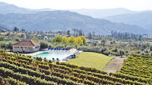A pool area with lounge chairs, a stone building, and vineyards in the foreground with mountains in the background. - Lam Hotel Convento do Desagravo (Oliveira do Hospital)