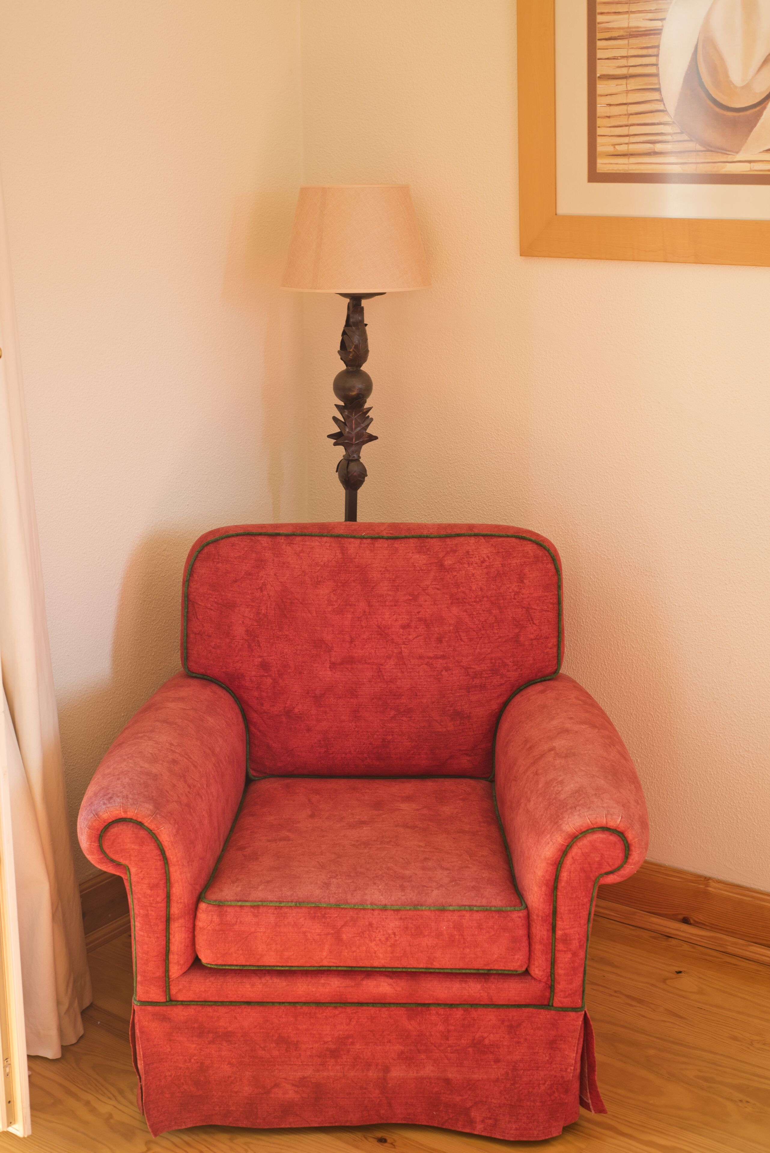 Un sillón rojo con detalles verdes, una lámpara y un cuadro en la pared.