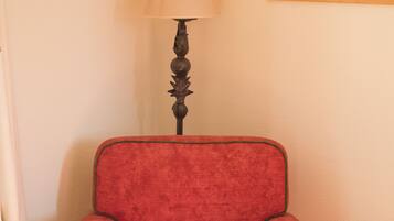 Un sillón rojo con detalles verdes, una lámpara y un cuadro en la pared.