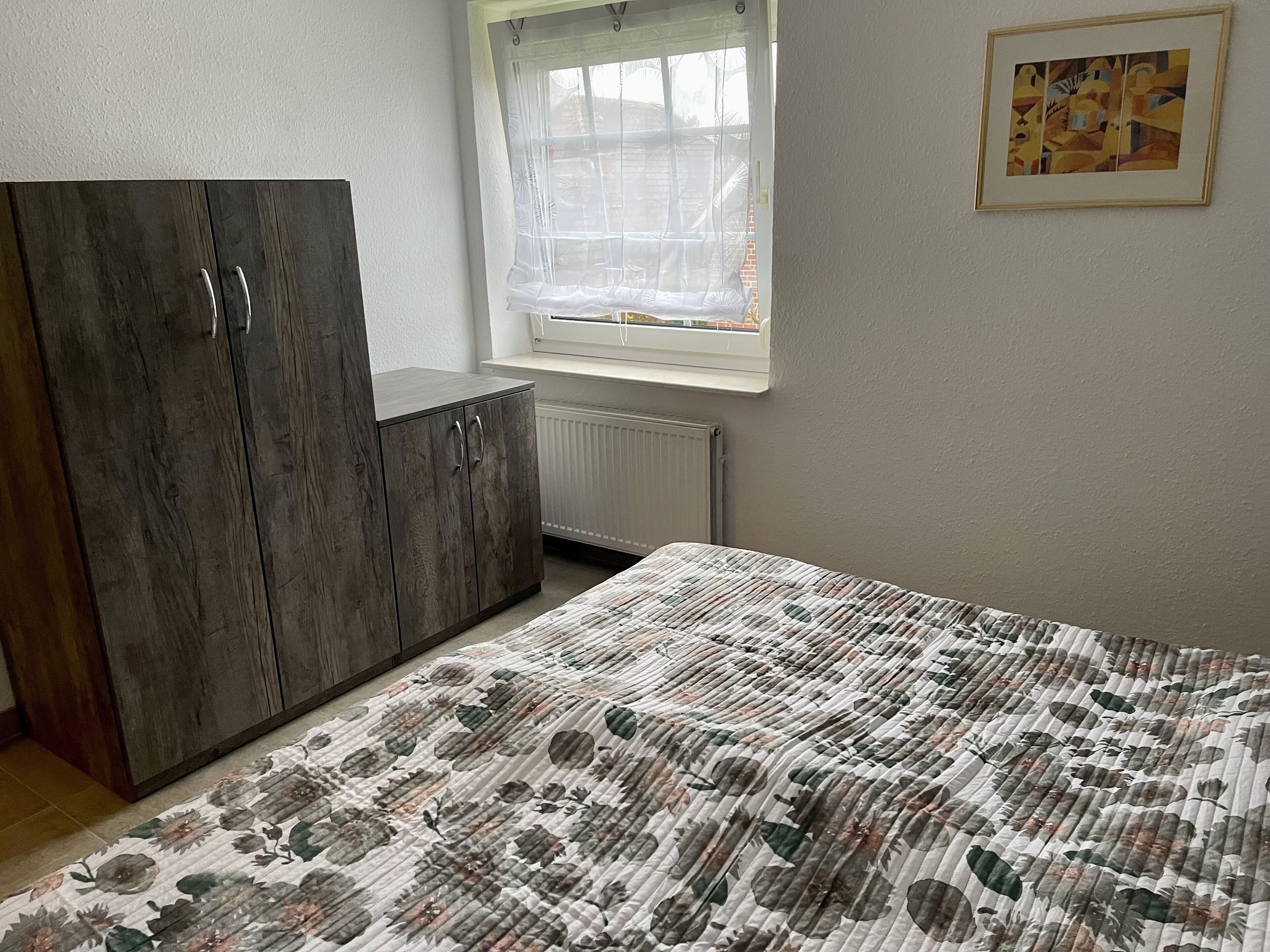 A bedroom with a bed, a wardrobe, a window with a view, and a radiator.