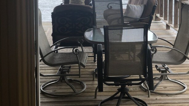 Ein überdachter Außenbereich mit zwei Stühlen und einem Tisch, mit Blick auf ein Gewässer.