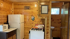 Eine kleine Küche mit Holzwänden, einem weißen Kühlschrank, einem Herd und einer Mikrowelle.