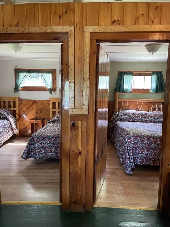 Una cabaña de madera con dos dormitorios, cada uno con cama y ventana con cortinas.