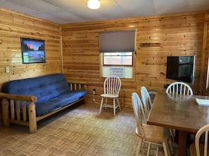 Cozy cabin-style room with a sofa, dining table, and TV, offering a view of the outside.