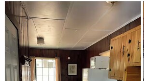Eine schmale Küche mit Holzvertäfelung, ausgestattet mit Kühlschrank, Spüle und Holzausstattung. Ein Fenster mit Vorhängen lässt natürliches Licht herein.