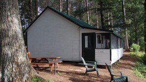Eine kleine Holzhütte mit einem grünen Dach, einer hölzernen Bank und zwei grünen Stühlen davor.
