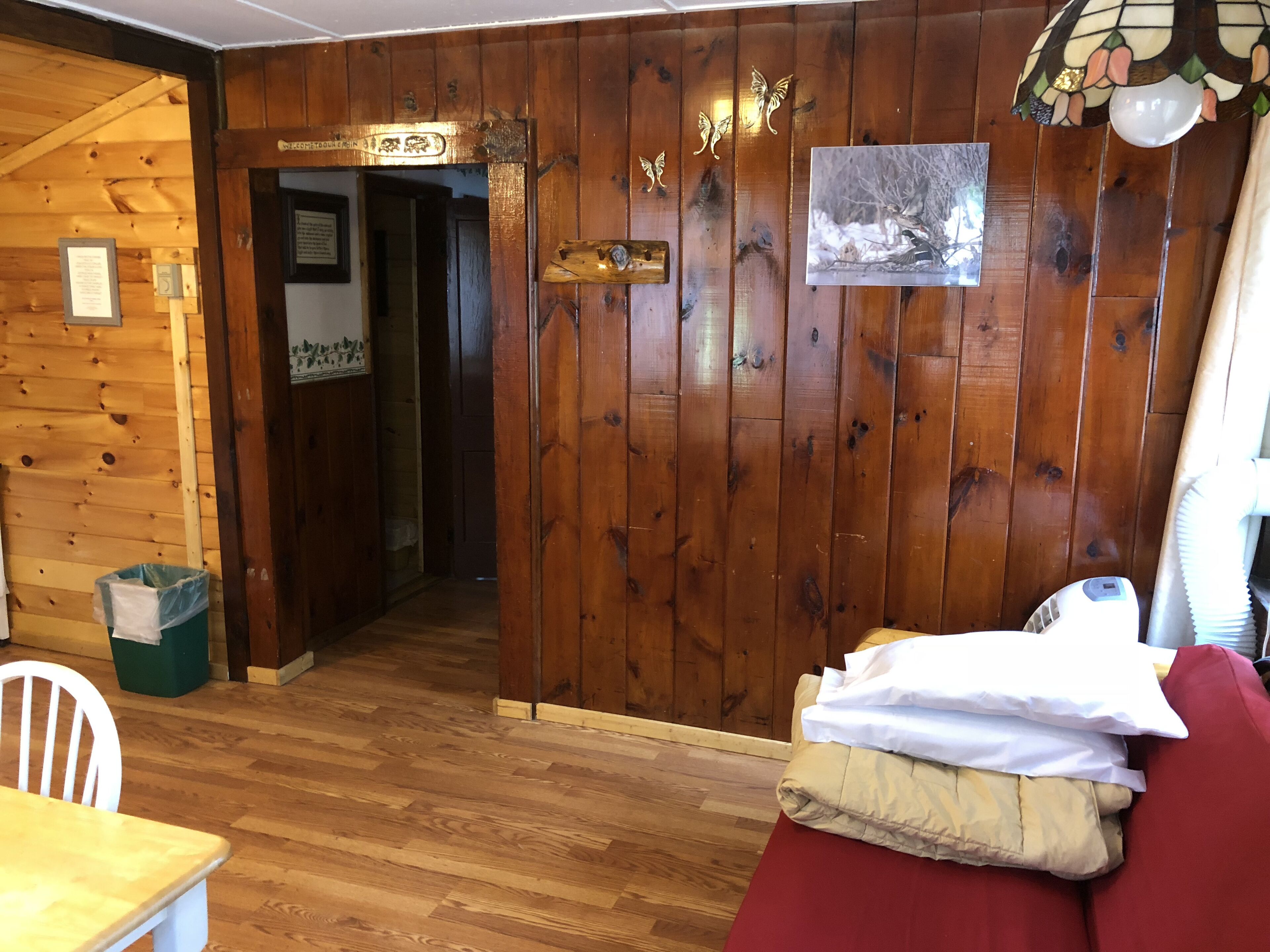 Un intérieur en bois avec une porte en bois, un tableau encadré au mur et un canapé rouge agrémenté de coussins.