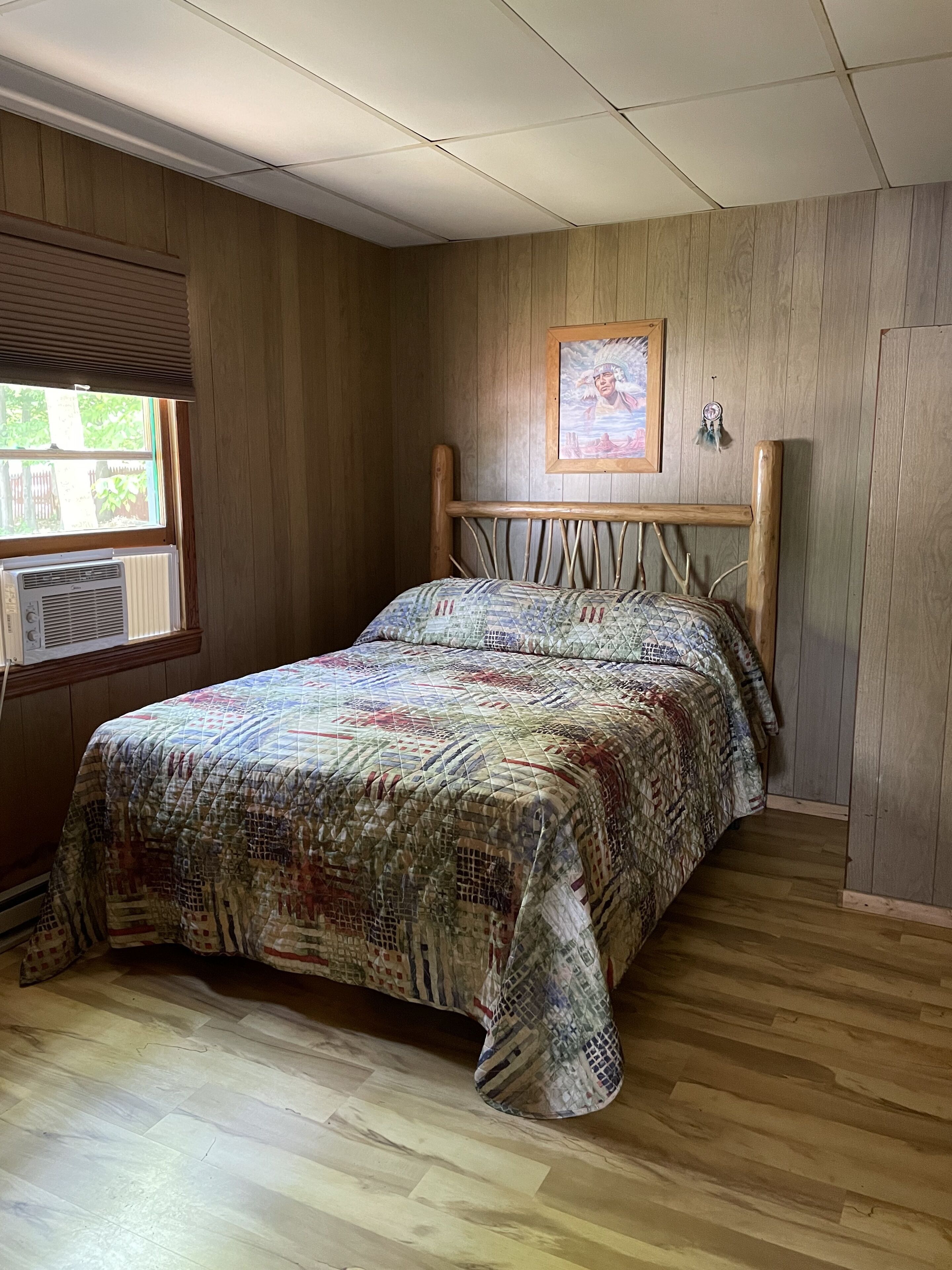 Ein Schlafzimmer mit einem hölzernen Kopfteil, einer gesteppten Bettdecke und einem Fenster mit Jalousien.