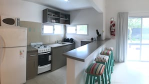 A kitchen with a refrigerator, stove, sink, and bar stools.