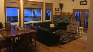 A cozy living room with a fireplace, wooden floors, and large windows with blinds.