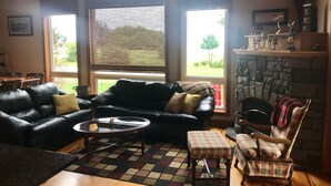 A cozy living room with a black leather sofa, a plaid armchair, and a small round table. A fireplace is visible in the background.