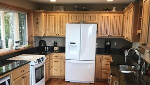 A kitchen with wooden cabinets, a refrigerator, stove, sink, and a window with curtains.