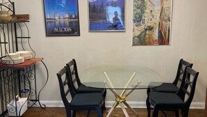 A dining area with a glass table surrounded by four chairs, a chandelier, and three framed pictures on the wall. - 50's Classic: Cozy, convenient, comfortable (St Louis)