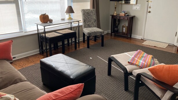 A living room with a sofa, ottoman, and a chair with a zebra print. There is a small table with a lamp and a decorative item. - 50's Classic: Cozy, convenient, comfortable (St Louis)
