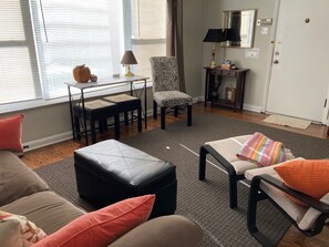 A living room with a sofa, ottoman, and a chair with a zebra print. There is a small table with a lamp and a decorative item. - 50's Classic: Cozy, convenient, comfortable (St Louis)