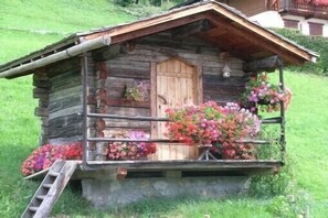 Una cabaña rústica de troncos con puerta de madera, un pequeño porche con arreglos florales y una escalera de madera.