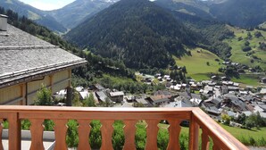 Un pueblo de montaña con casas tradicionales, un balcón de madera y vistas de las colinas circundantes.