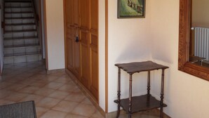 Una habitación con techo de madera, una escalera, una puerta de madera, un cuadro enmarcado, una mesita y un radiador.