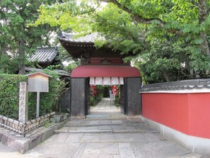 Une porte traditionnelle japonaise, avec un toit rouge et des marches en pierre menant à l’intérieur.