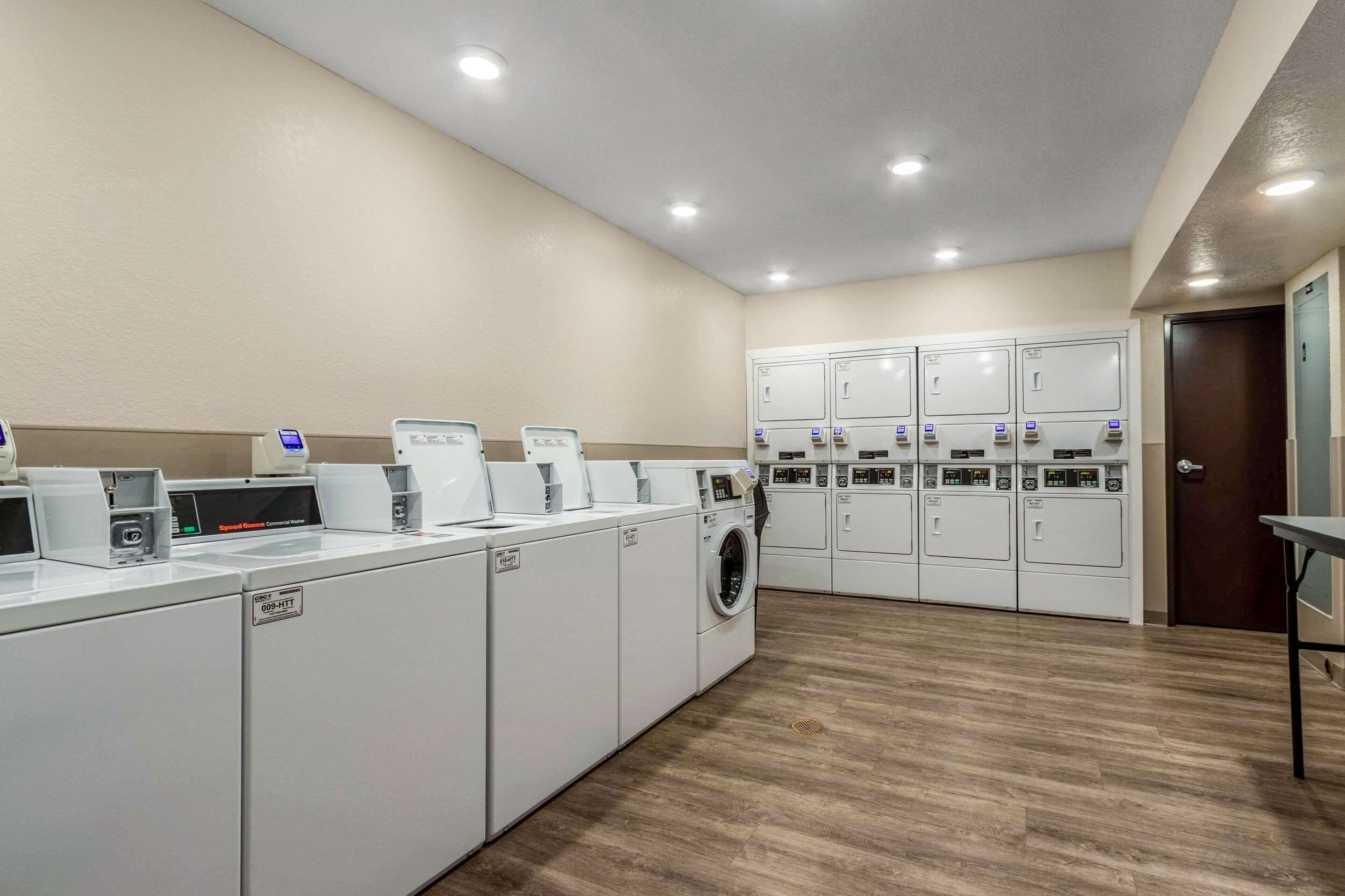 A laundry facility with multiple washing machines and dryers, a control panel, and a wooden floor.