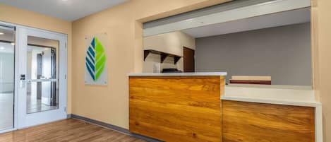 A reception area with a wooden reception desk, a glass door entrance, and a green leaf-shaped decoration on the wall.