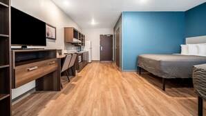 Ein gemütliches Zimmer mit Bett, Schreibtisch, Stuhl, Fernseher und einer Küchenzeile.