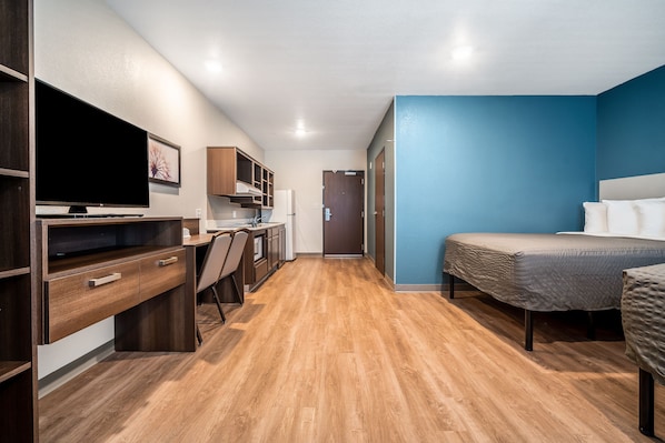 Une petite chambre comprenant un lit, un bureau, une chaise, un téléviseur et un coin cuisine.
