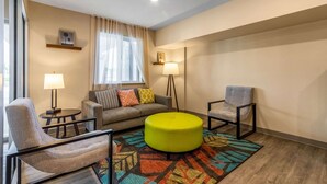 Ein modernes Wohnzimmer mit einer Couch, zwei Sesseln, einem runden Hocker, einem gemusterten Teppich und zwei Stehlampen.