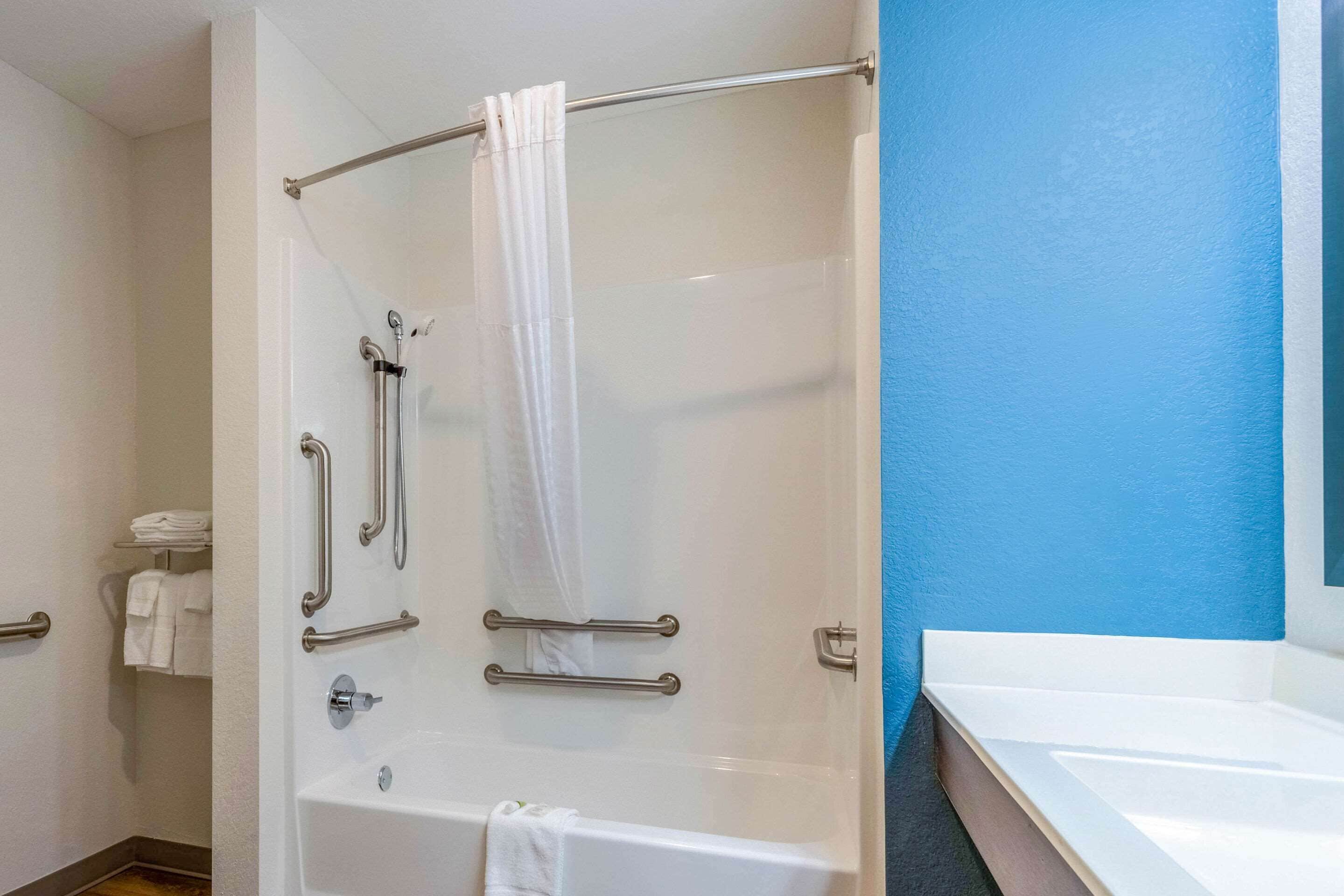 A bathroom with a bathtub, a shower with grab bars, and a towel rack.