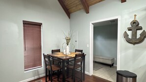Uma área de refeições com mesa e cadeiras de madeira, uma planta em vaso e uma lixeira.