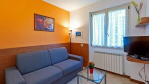 A living room with a sofa, a TV, a lamp, and a window with curtains. - Lake Como - Residence La Collina - Pera (Vercana)