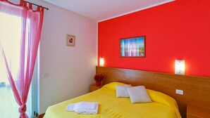 A hotel room with a yellow bed, red walls, a framed picture, and a window with pink curtains. - Lake Como - Residence La Collina - Pera (Vercana)