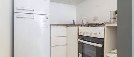 A compact kitchen with a white refrigerator, a stove with four burners, and a microwave.