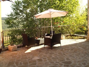 Un patio al aire libre con suelo de piedra, mobiliario de mimbre y una mesa con copas de vino.