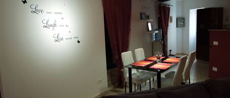 A dining area with a table set for four, white chairs, and a red curtain.