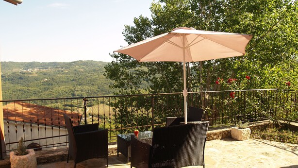 A patio with stone flooring, two wicker chairs, a table, and a large beige umbrella. - Provvidenza (Motovun)