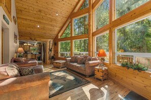A spacious living room with a large wooden ceiling, multiple windows, a fireplace, and a cozy seating area.