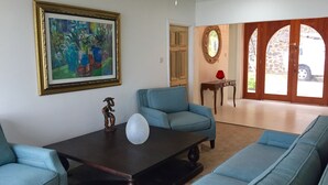 A living room with a dark wooden coffee table, two blue sofas, a framed painting, a small wooden figurine, and a door leading to an outdoor area with a stone wall and a vehicle parked outside. - Tropical, Romantic and  Chic at Marisule Villa (Gros Islet)