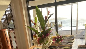A wooden table with a vase of flowers and patterned placemats, set against a large window overlooking the sea. - Tropical, Romantic and  Chic at Marisule Villa (Gros Islet)