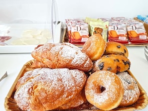 A tray of assorted pastries including bread and doughnuts, with a clear plastic container and packets of Le Dorate in the background. - Villa Susy Relais (Sant'Agnello)