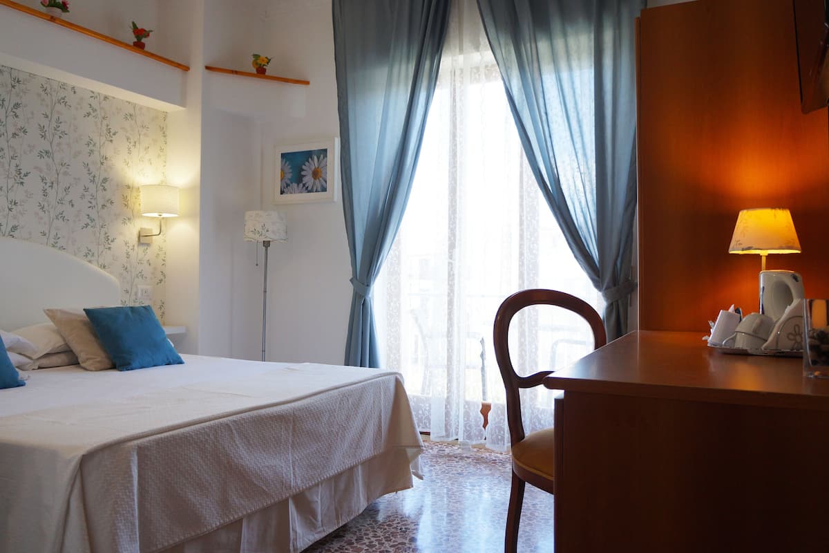 A hotel room with a bed, a desk with a lamp, and a chair.