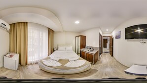 Habitación de hotel con una cama curvada, un escritorio pequeño, una tocador con lavabo y un televisor montado en la pared.